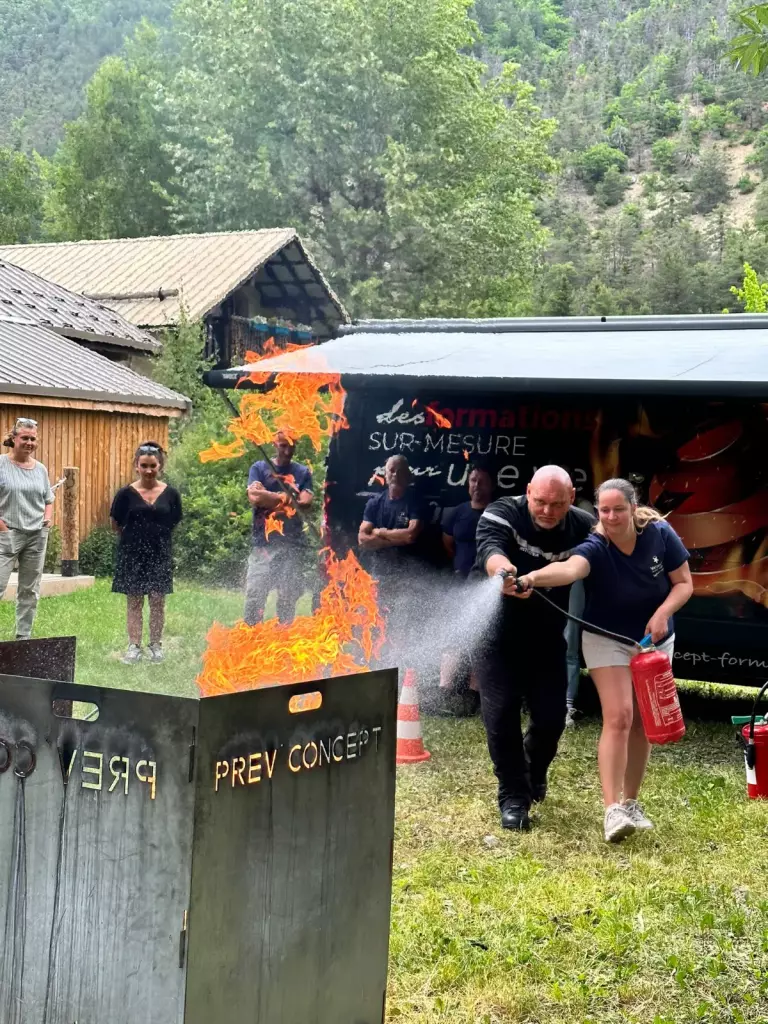 Stagiaire utilisant un extincteur sur un bac à feu, guidée par un formateur Prev’Concept, lors d’une formation incendie dans un camping